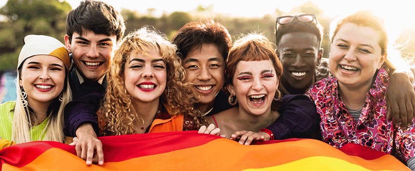 A group of students holding a rainbow flag smiling.